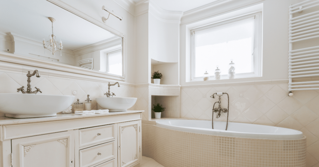 corner shot of a bathroom with neutral colour tones showing a bath, sink, window and a mirror